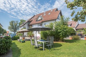 A residential area with a house featuring a sloped roof, a patio with a table and chairs, and a lawn.