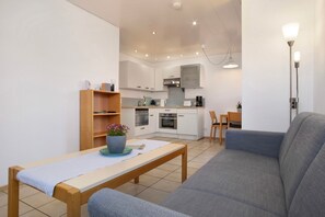 A modern kitchen with white cabinets, a dining area with a wooden table and blue sofa, and a small seating area with a chair.
