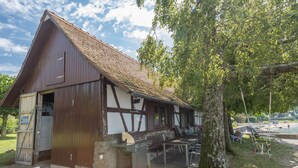 A traditional building with a sloped roof, a wooden door, and a barbecue area with a grill and seating.