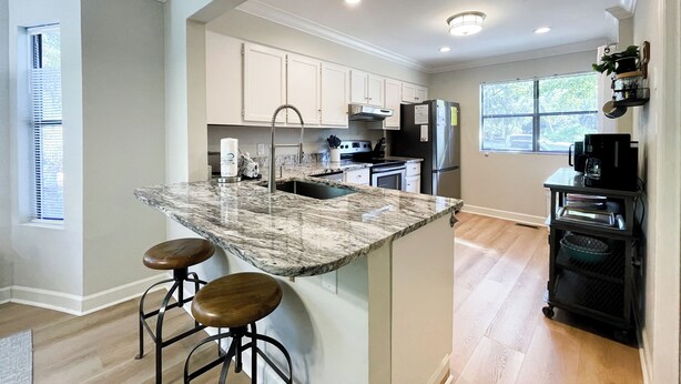 A modern kitchen with white cabinets, a marble island with stools, and a black refrigerator.