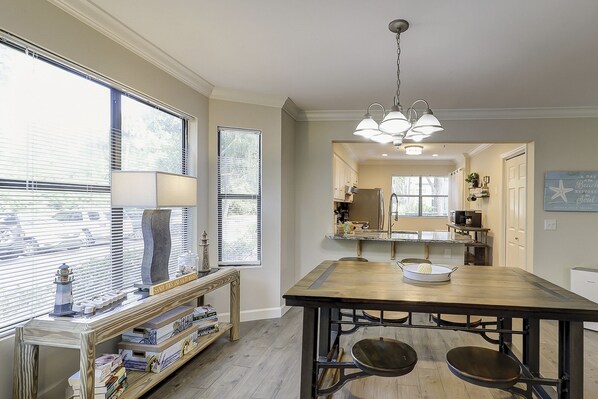 Une cuisine avec une table en bois, un luminaire suspendu et une vue sur l’extérieur grâce à de grandes fenêtres.