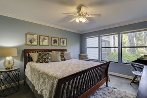 A bedroom with a bed, a ceiling fan, a window with blinds, and a nightstand with a lamp.