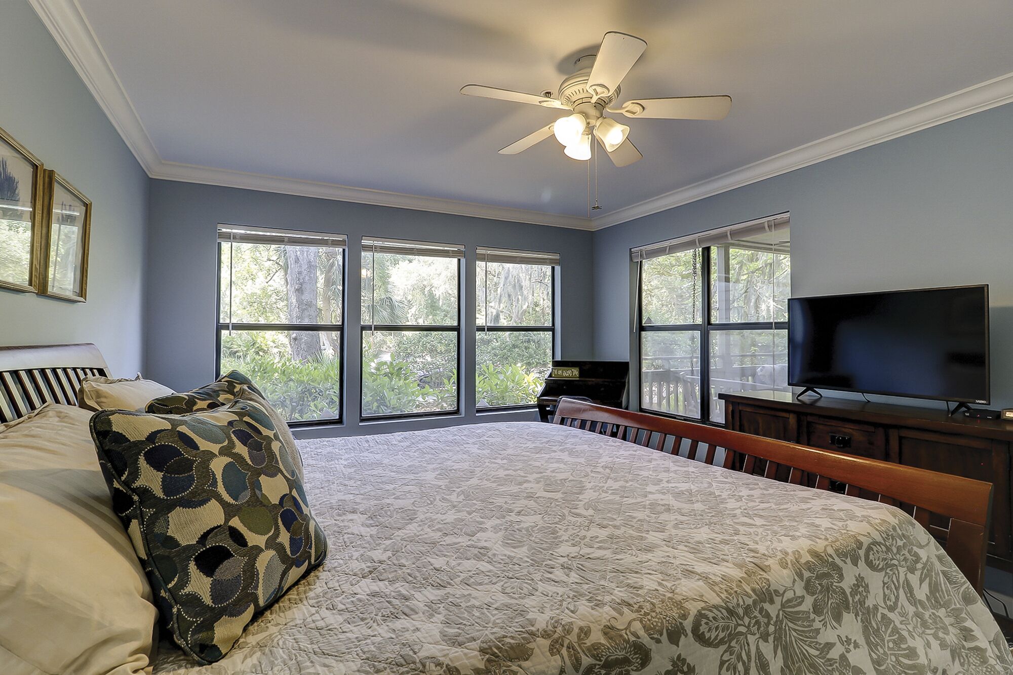 A bedroom with a large bed, a ceiling fan, a TV, and a piano.