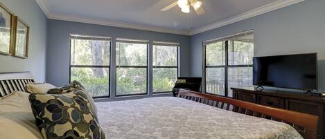 A bedroom with a large bed, a ceiling fan, a TV, and a piano.