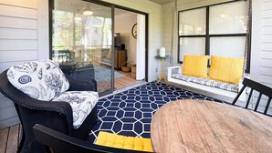A covered patio with a hexagonal patterned floor, a round wooden table, and a black and white patterned sofa.