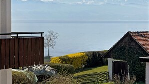 A view of a lake with mountains in the background, a wooden deck, and a small building with a sloped roof.