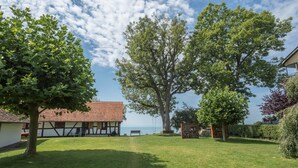 A courtyard with a large tree, a building with a tiled roof, and a view of the sea.
