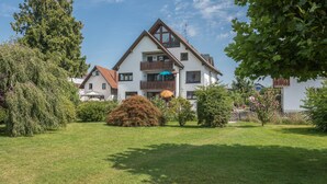 A two-story house with a large garden, a wooden fence, and a clear sky.