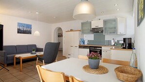 A modern kitchen with white cabinets, a dining table with chairs, a sofa, and a pendant light.