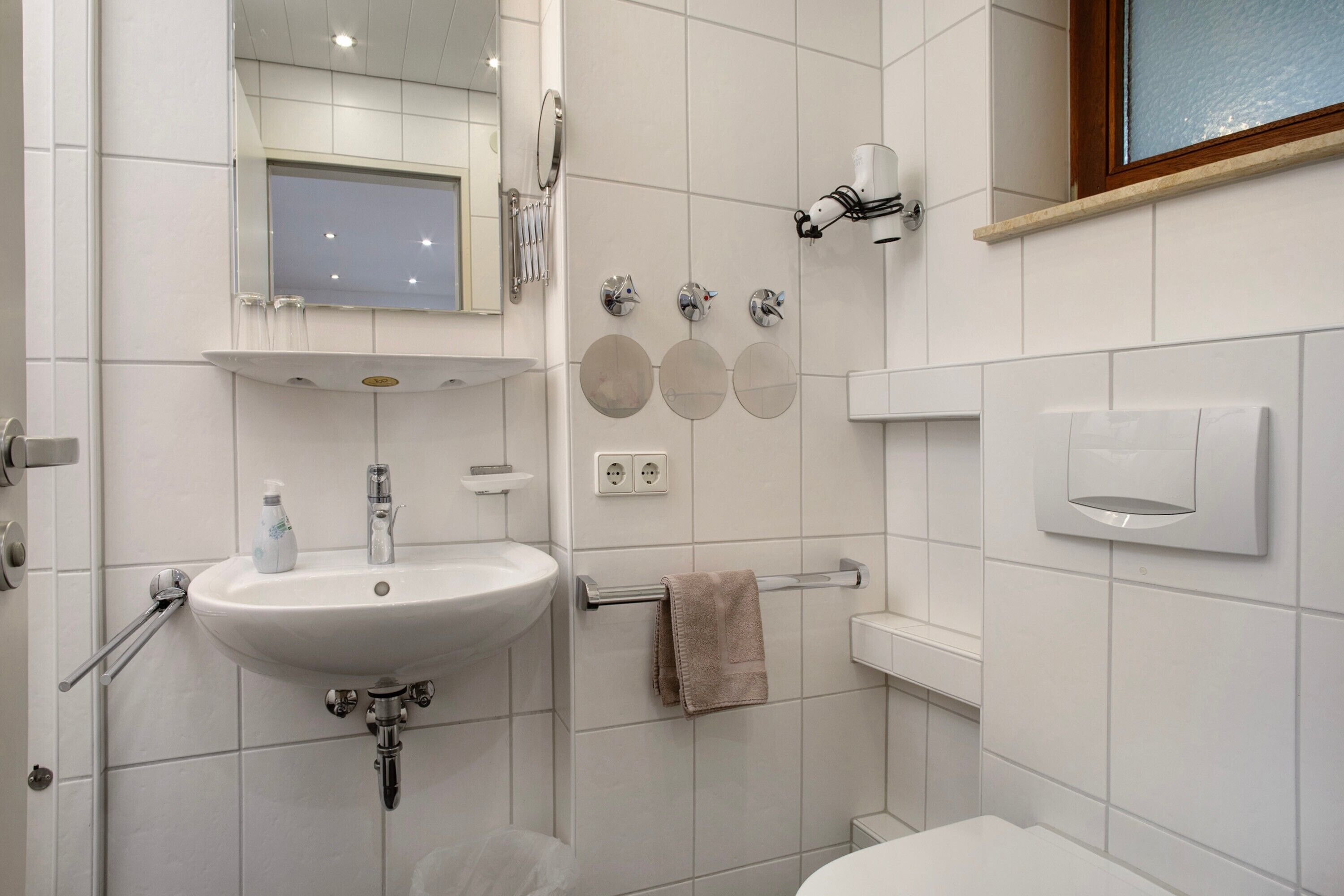 Une salle de bain équipée d’un lavabo, d’un miroir, d’un porte-serviettes et d’un distributeur de savon.