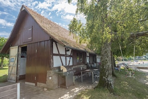 A rustic building with a sloped roof, a wooden door, and a barbecue grill outside.