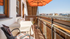 Un balcon avec une table et des chaises, un parasol et une vue sur les bâtiments au loin.