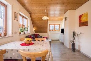 Un coin repas avec une table dressée pour deux personnes, un canapé et un téléviseur en arrière-plan.