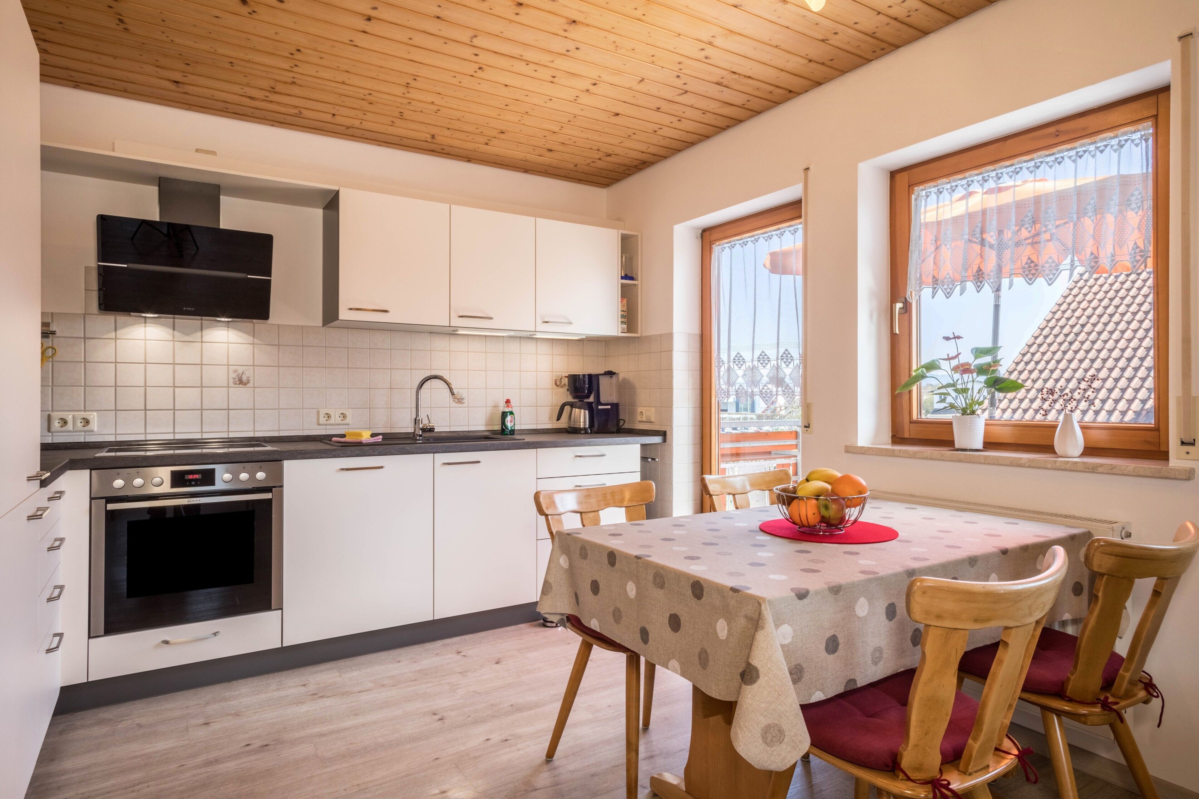 Eine moderne Küche mit weißen Schränken, einer Holzbalkendecke und einem Essbereich mit gedecktem Tisch für zwei Personen.