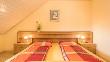 Ein Schlafzimmer mit Holzboden, einem Bett mit Karo-Bettwäsche, zwei Nachttischlampen, einem Nachttisch und einem gerahmten Bild an der Wand.
