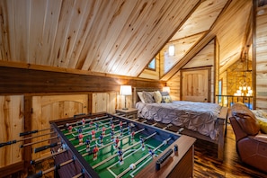 Une pièce chaleureuse, avec des murs en bois, comprenant une table de baby-foot, un lit et un coin salon.
