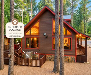 A wooden cabin with a fenced dog run, surrounded by trees. - Pet-Friendly Broken Bow Cabin on Stream with Hot Tub, Dog Run & Game Room (Broken Bow)