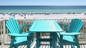 Terraza turquesa con mesa y sillas que da a una playa con sombrillas y gente.