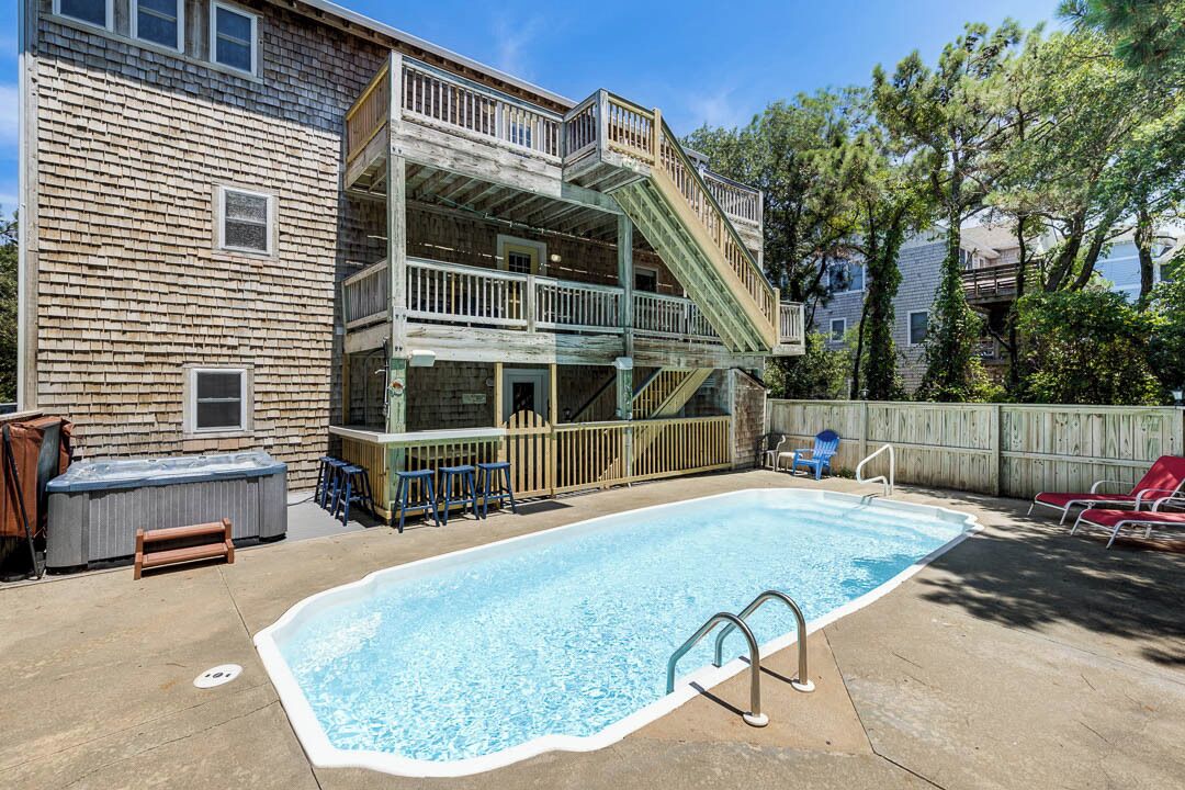 Un patio trasero con piscina, jacuzzi y terraza de madera con escalera.