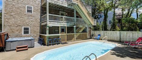 A backyard with a swimming pool, a hot tub, and a wooden deck with a staircase.