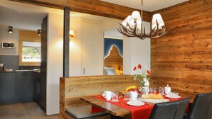 A dining area with a wooden bench, a table set for two with a red table runner, and a chandelier with antler-shaped light fixtures. - Cosy apartment for 4 people with WIFI, TV and balcony (Zermatt)