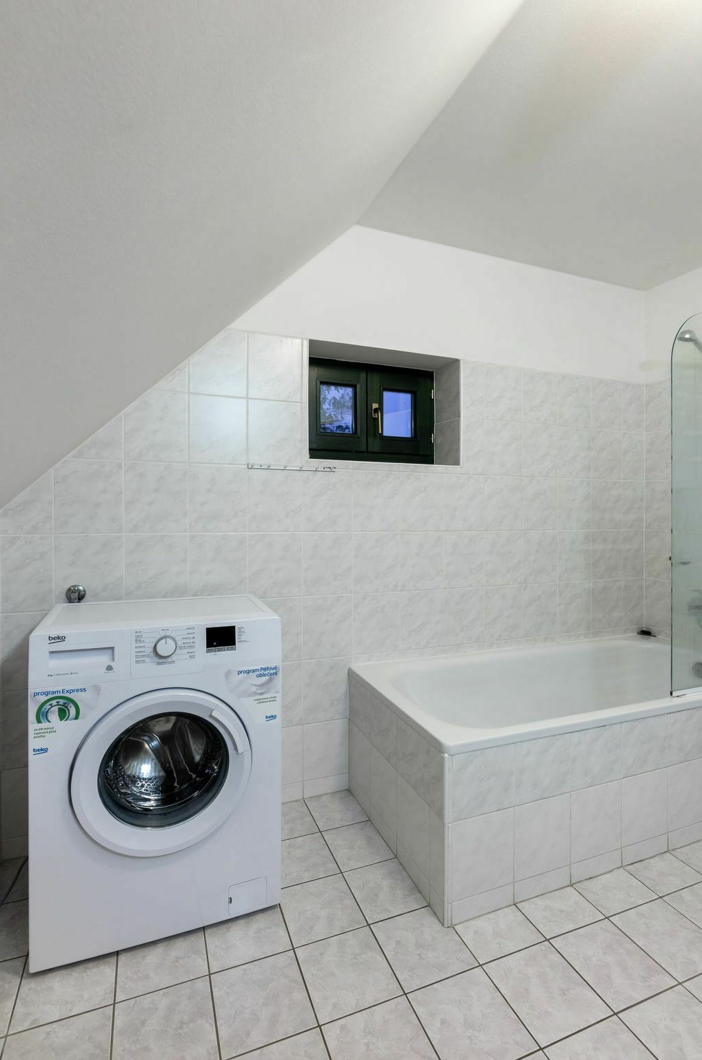 A modern bathroom with a washing machine, a bathtub, and a small TV mounted on the wall.