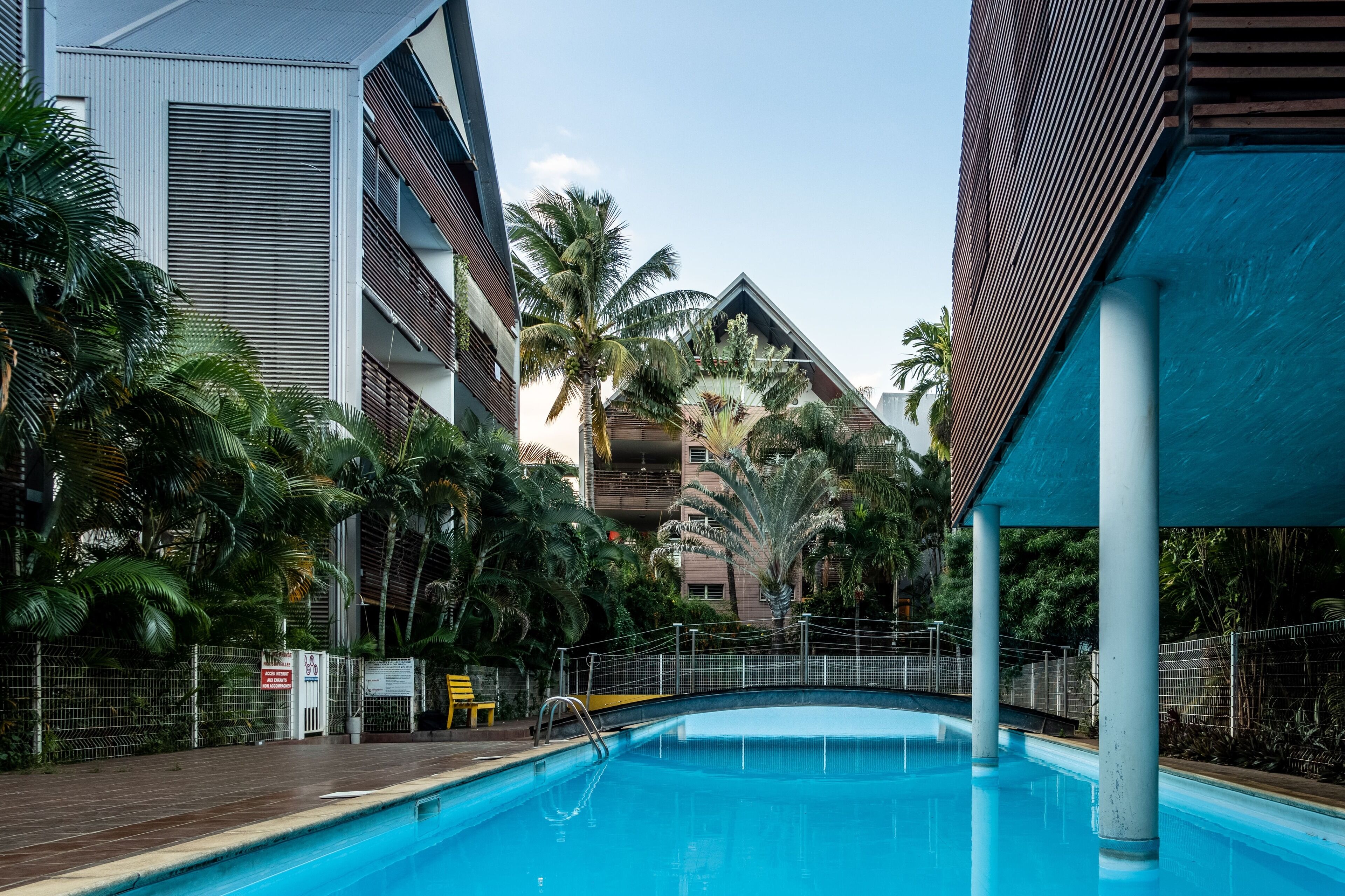 Une piscine entourée d’une végétation luxuriante et de bâtiments modernes.