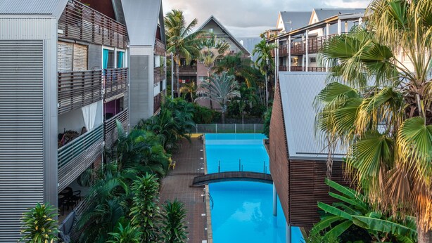 Ein modernes Hotel mit einem zentral gelegenen Schwimmbad, umgeben von üppiger Vegetation und Palmen.