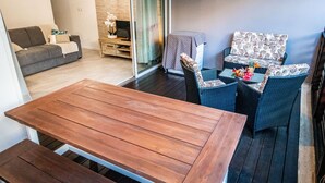 Ein Wohnbereich mit einer Couch, einem Holztisch, Korbstühlen und einem Fernseher.