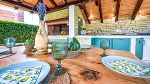 An outdoor dining area with a wooden table set for a meal, surrounded by a brick wall and a wooden ceiling. - Apartment Petra by Interhome (Biograd na Moru)