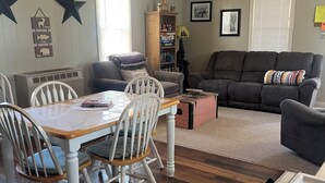 Una sala de estar acogedora con chimenea, un comedor con mesa y sillas de madera, y una cocina con estufa.