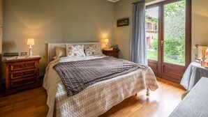 A bedroom with a bed, bedside tables, a window with curtains, and a view of greenery outside.