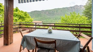 A covered outdoor dining area with a checkered table and chairs, overlooking a mountainous landscape.