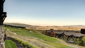 A golf course with a view of distant mountains, a stone wall, and a row of wooden buildings.
