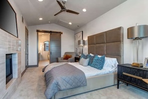 Um quarto moderno com cama, mesa de cabeceira, luminária, ventilador de teto e lareira.