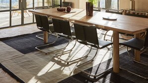 A dining area with a large table, chairs, and a view through a large window.