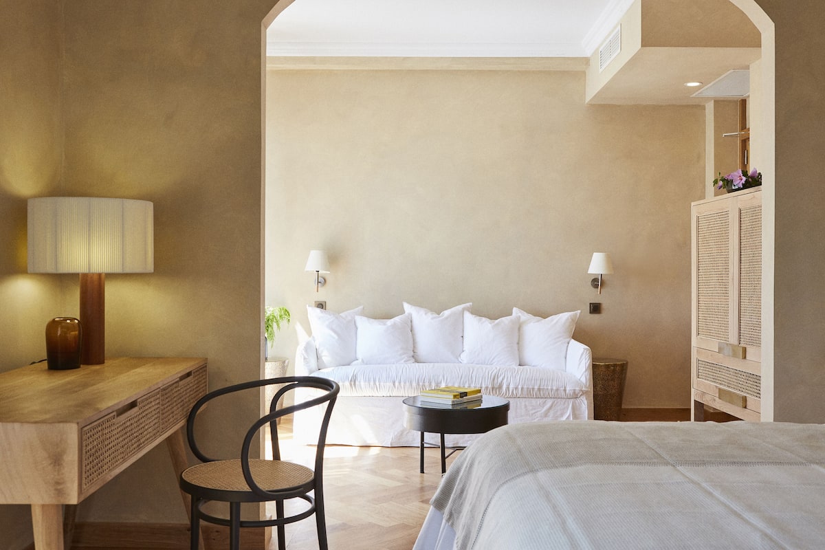 Une chambre d’hôtel comprenant un lit, un bureau avec une lampe, une chaise, une petite table et une armoire.