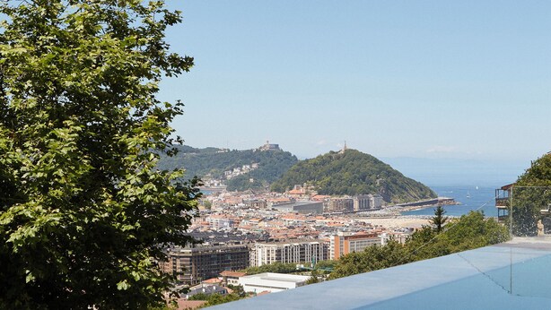 A clear view of a swimming pool with a cityscape in the background, including buildings and a hill.