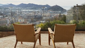 Two wicker chairs on a brick patio overlooking a cityscape with mountains in the distance.