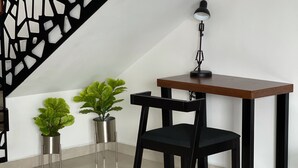 Una habitación moderna con un escritorio de madera, una silla negra, una lámpara de pie y dos plantas en macetas.