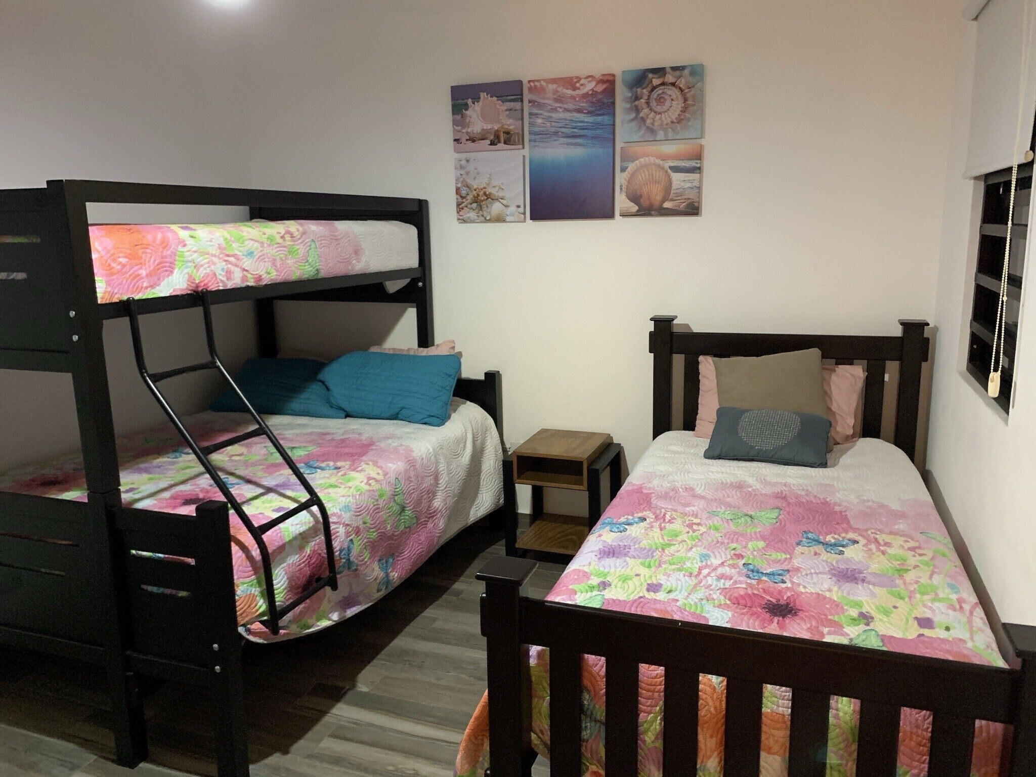 Ein Zimmer mit Etagenbetten, einem kleinen Nachttisch und einer Wand mit vier gerahmten Bildern.