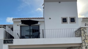 Una casa moderna de dos pisos con balcón, un muro de piedra y una entrada con tejas.