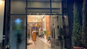 The entrance to a restaurant named 'TWINS' with a modern design, featuring glass doors, indoor lighting, and potted plants.