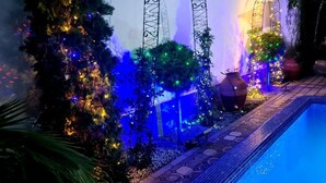 A poolside area with a tiled edge, decorative arches, and a Christmas tree adorned with lights.