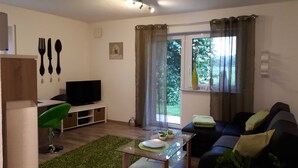A modern living room with a flat-screen TV, a green chair, a glass coffee table, and a sofa with cushions. - Ferienwohnung Riesling - Weinlodge am Geissberg (Eberstadt)