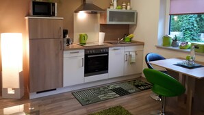 A modern kitchen with a microwave, stove, oven, and a sink. There is a dining area with a chair and a table. - Ferienwohnung Riesling - Weinlodge am Geissberg (Eberstadt)
