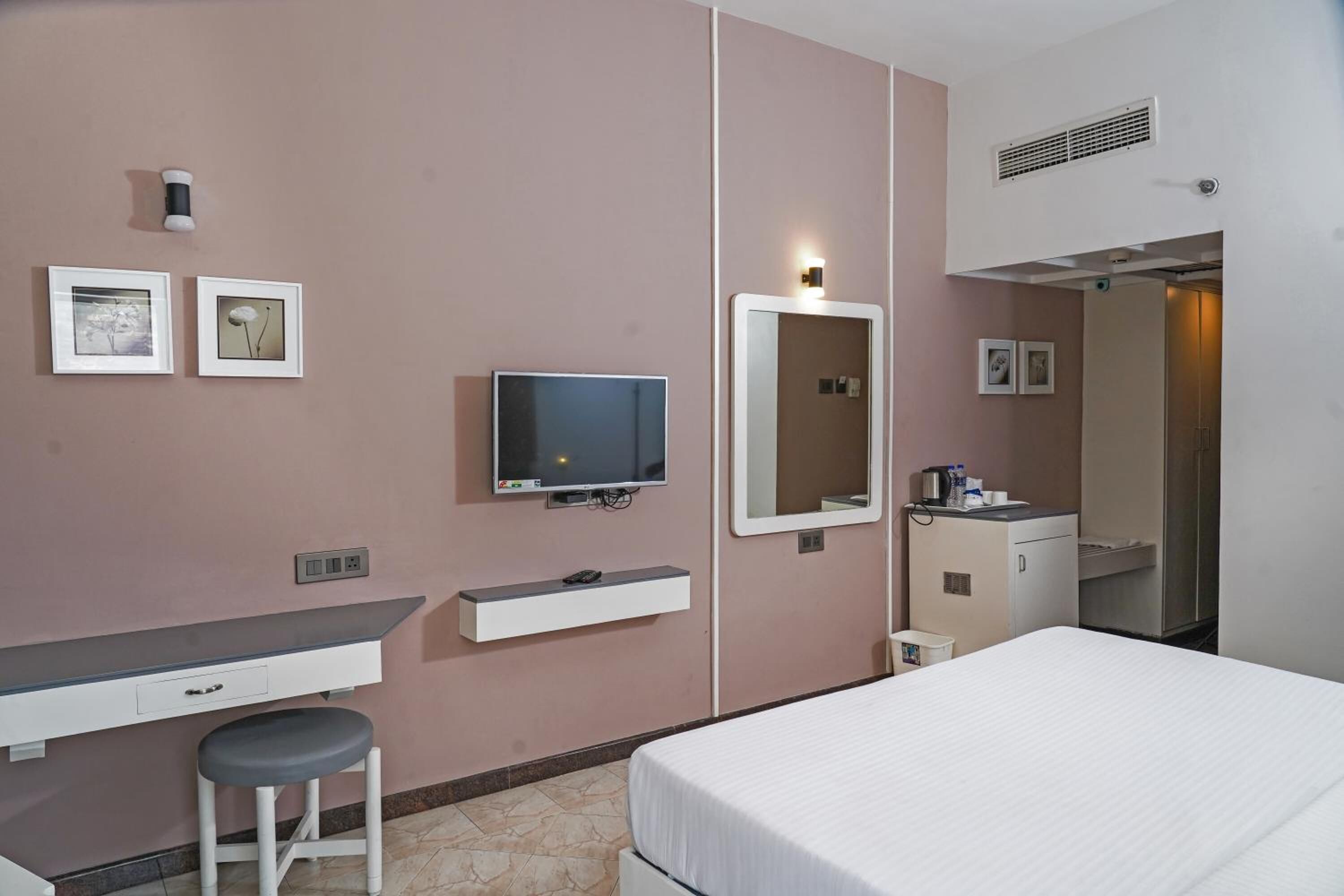 A hotel room with a bed, a desk with a chair, a television, a mirror, and a small cabinet.