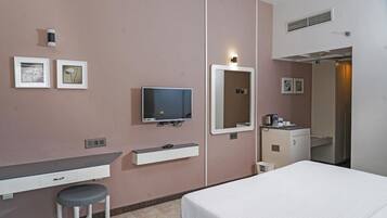 A hotel room with a bed, a desk with a chair, a television, a mirror, and a small cabinet.