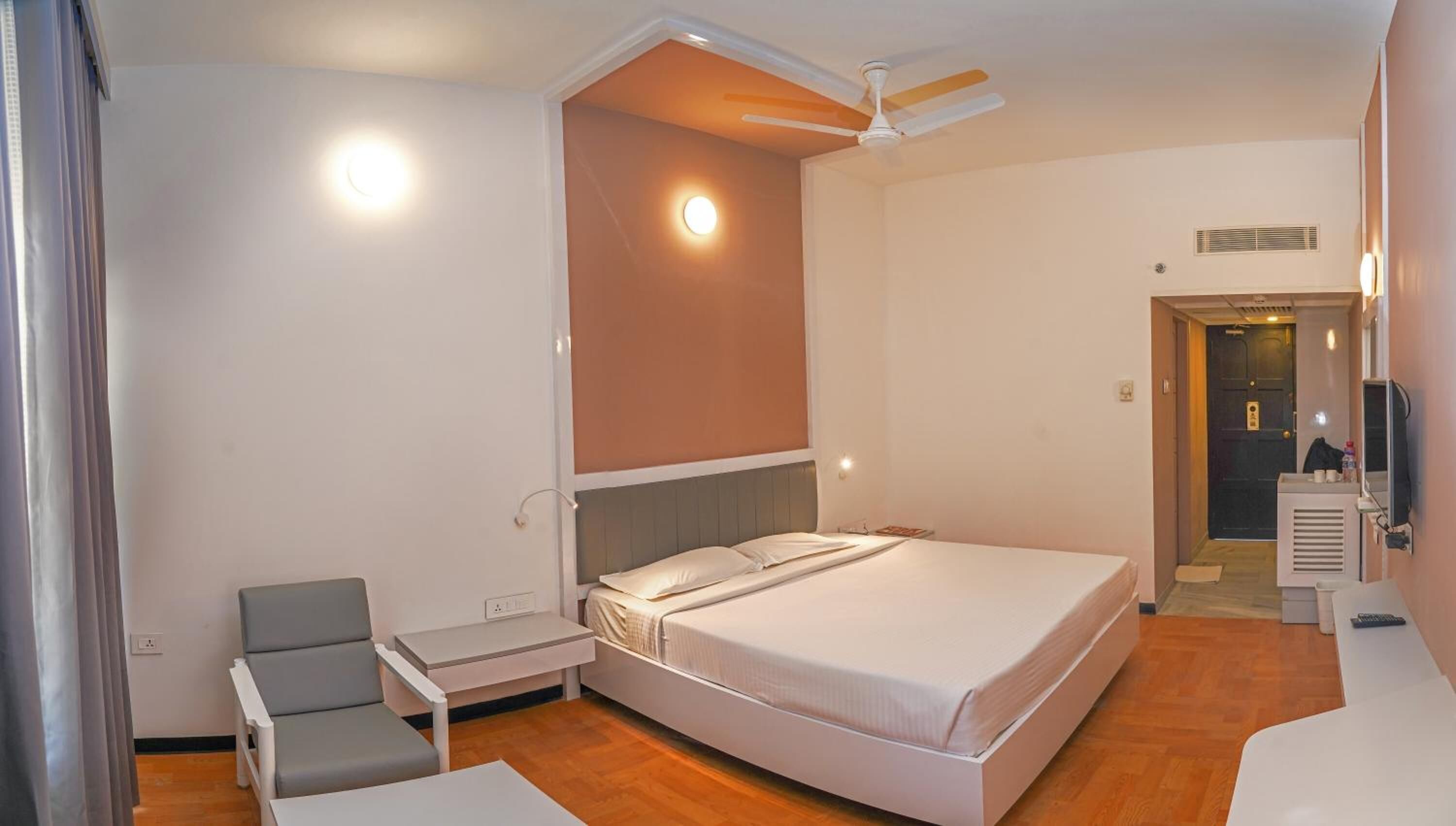 Ein modernes Hotelzimmer mit einem großen Bett, einem Schreibtisch, einem Stuhl, einem Deckenventilator und einem Fernseher.