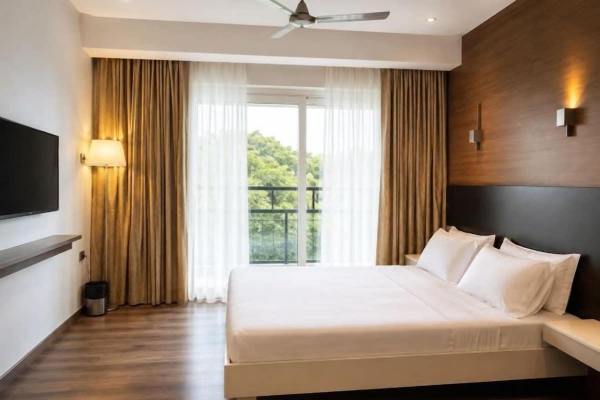 A hotel room with a bed, curtains, a ceiling fan, a TV, and a balcony view.
